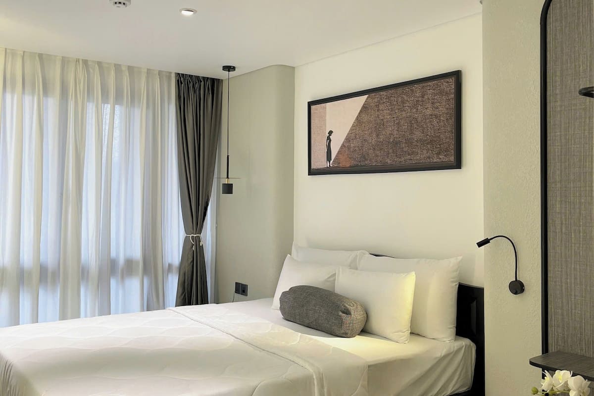 Une chambre d’hôtel moderne avec un lit bien fait, un bureau avec une chaise et une grande fenêtre avec des rideaux.