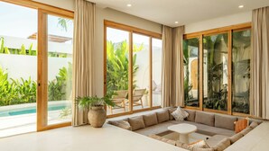 Ein modernes Wohnzimmer mit einem beigen Sofa, einem weißen Couchtisch und einer großen Glasschiebetür zum Poolbereich.