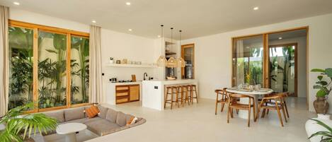 A modern living room with a sofa, a dining table with chairs, and a kitchen area with a bar stool.