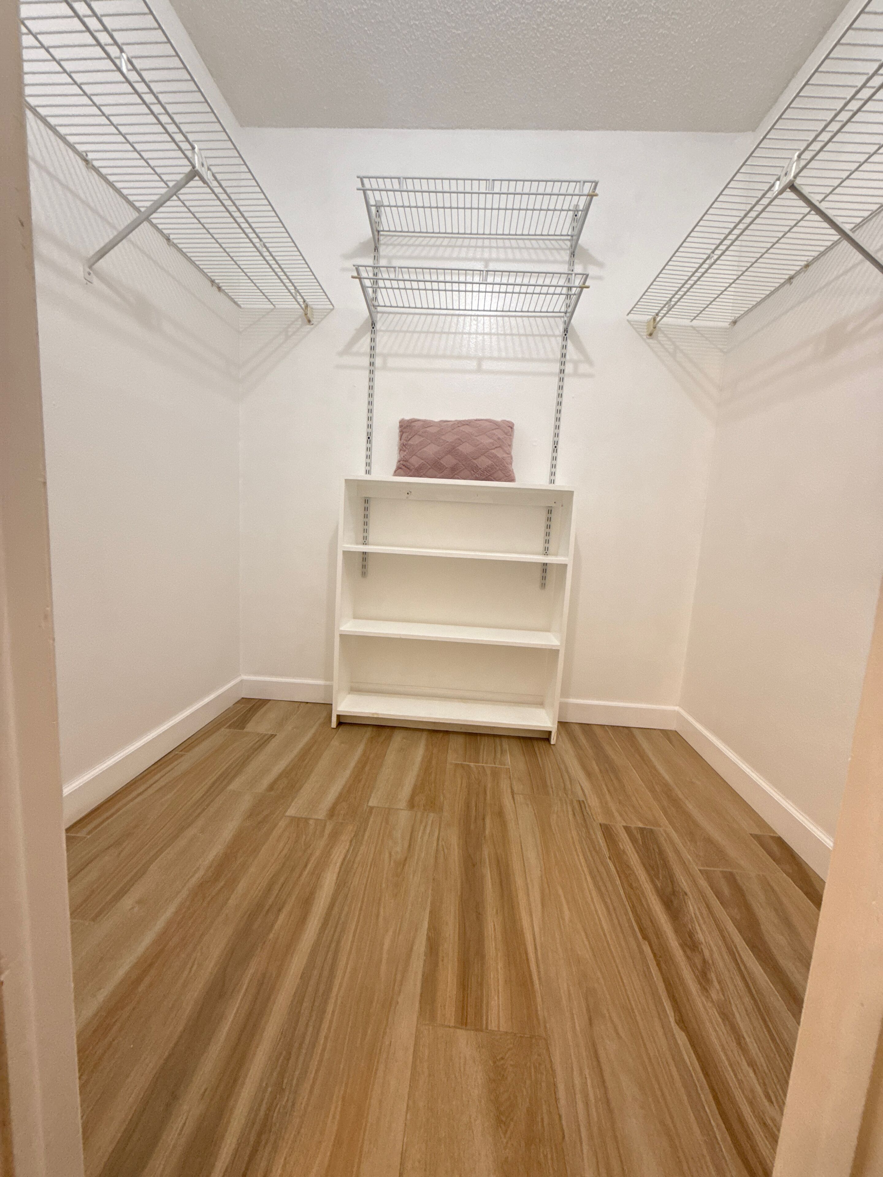 Ein begehbarer Kleiderschrank mit Holzboden, weißen Wänden und Metallregalen.