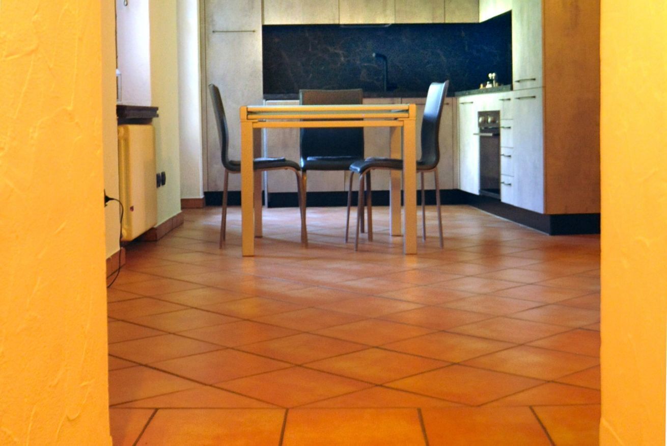 Een keuken met een eettafel en stoelen, een betegelde vloer en keukenkastjes.