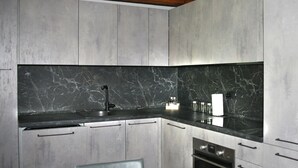 A modern kitchen with a marble countertop, stainless steel appliances, and a wooden ceiling beam.