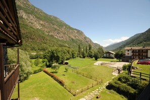 A mountainous landscape with a well-maintained garden, a wooden fence, and a building with a sloped roof.