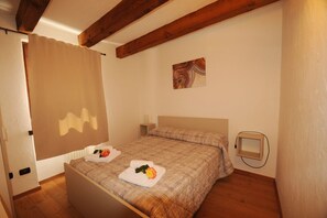 A bedroom with a bed, wooden beams, a painting, and a bedside table.
