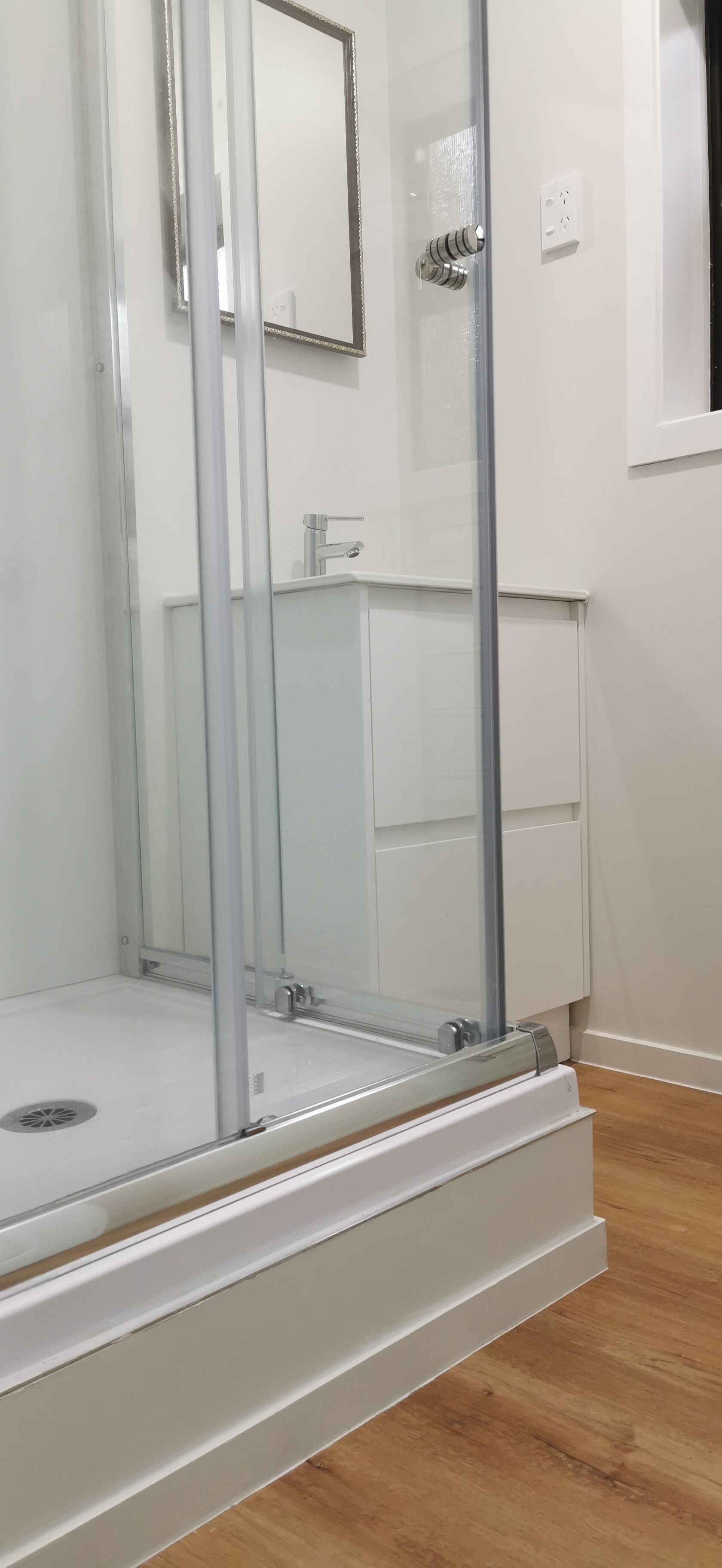 A bathroom with a glass shower enclosure, a white cabinet, and a mirror.