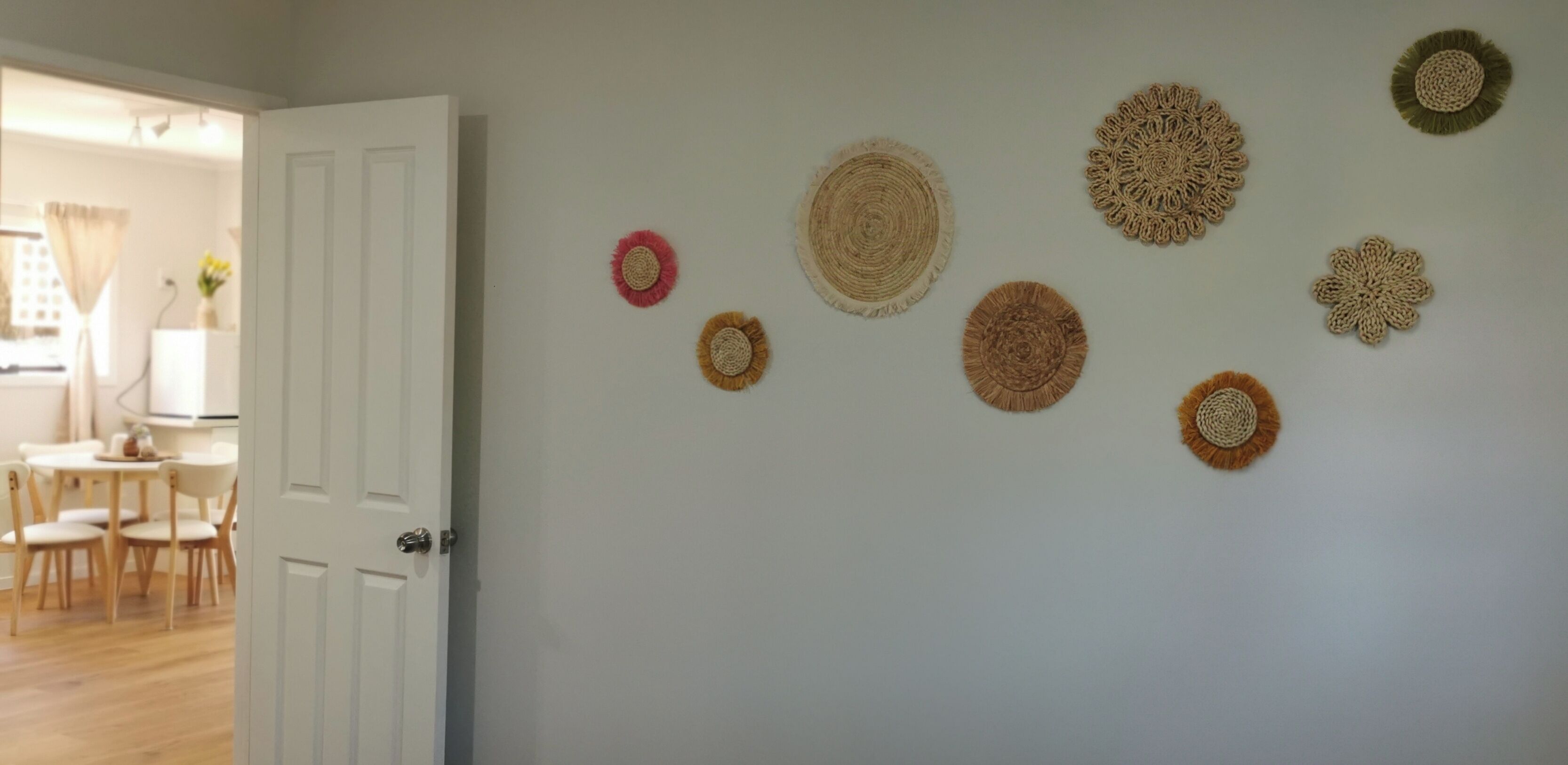 A room with a white door, a dining area with a table and chairs, and a wall decorated with circular woven art pieces.