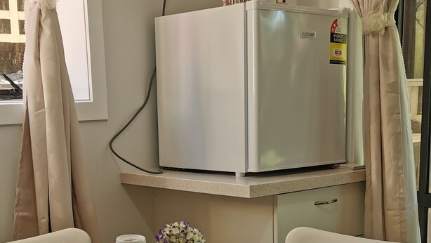 Een eetgedeelte met een ronde tafel, witte stoelen, een koelkast en een vaas met bloemen.