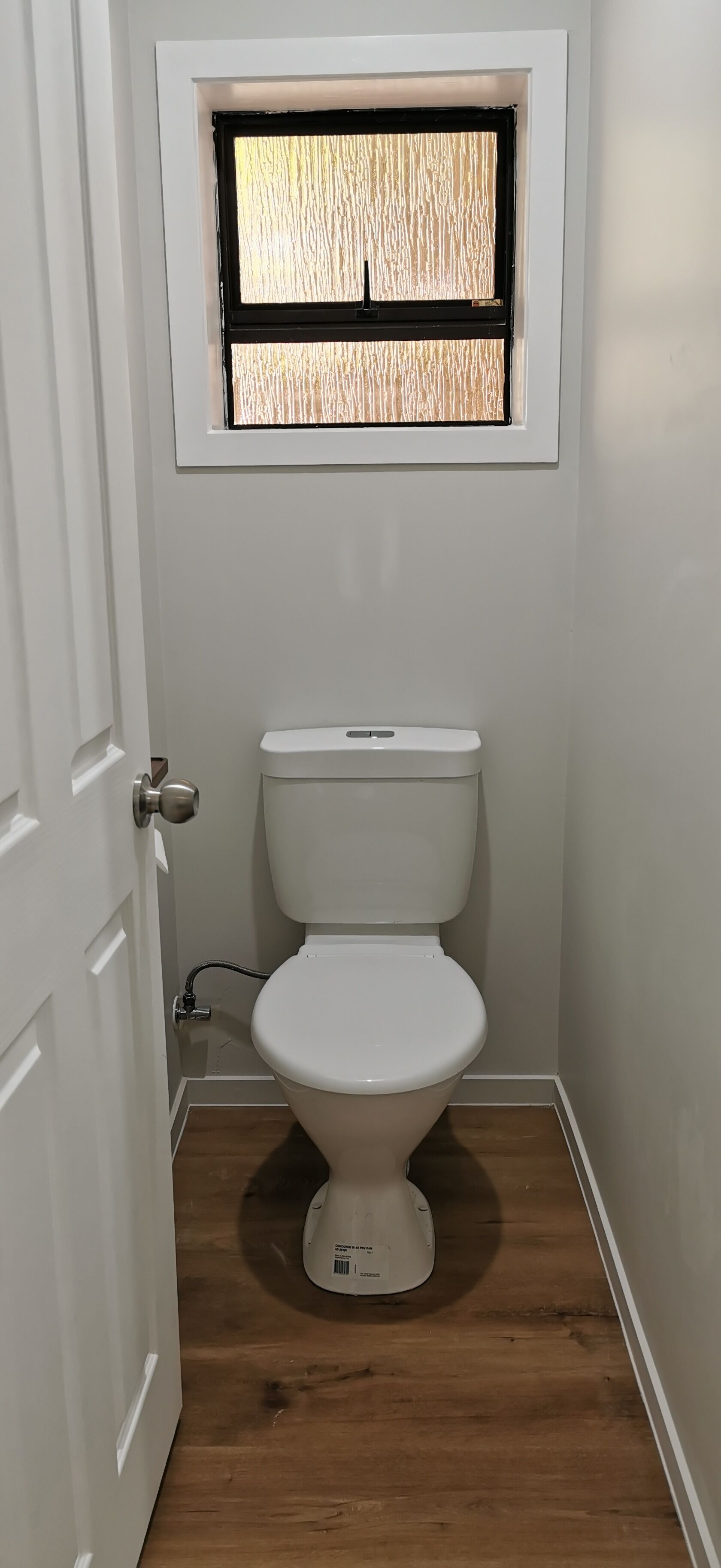 A small, clean bathroom with a toilet, a window above it, and a wooden floor.