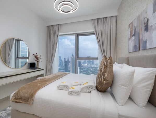 Une chambre d’hôtel moderne, dotée d’un grand lit, d’un bureau avec un ordinateur portable et offrant une vue sur le paysage urbain par la fenêtre.