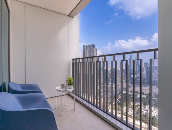 Ein Balkon mit zwei blauen Stühlen, einem kleinen Tisch mit einer Pflanze und Blick auf eine Skyline mit hohen Gebäuden.