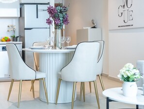 Eine moderne Küche mit einem weißen Esstisch, zwei weißen Stühlen mit goldenen Beinen und einer Vase mit violetten Blumen.