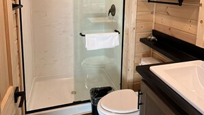 A modern bathroom with a glass-enclosed shower, a white toilet, and wooden cabinetry.