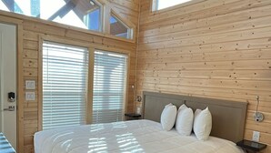 A bedroom with a large bed, wooden walls, a ceiling fan, and skylights.