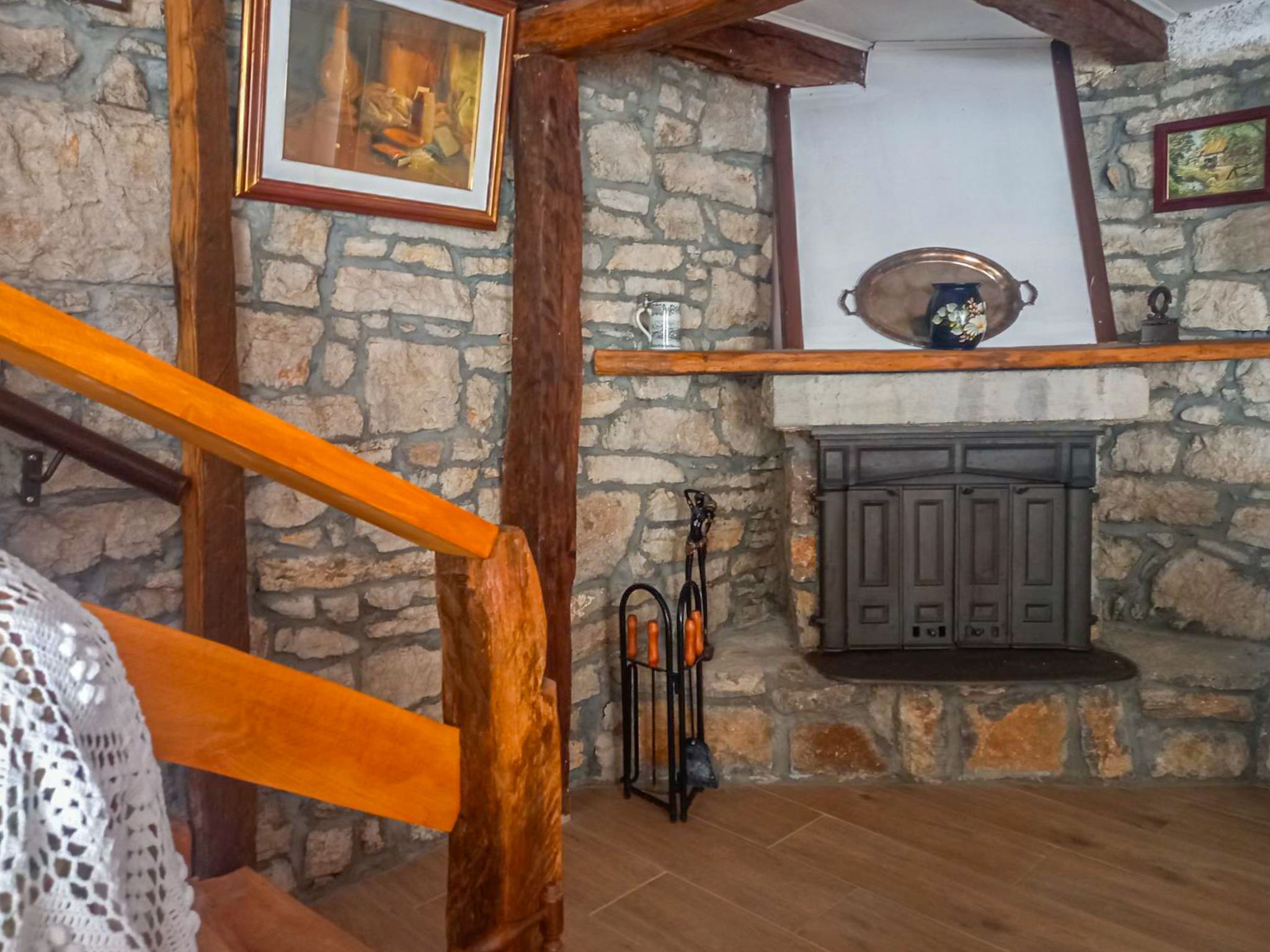 A rustic interior with a stone wall, wooden beams, a fireplace, and a framed picture on the wall.