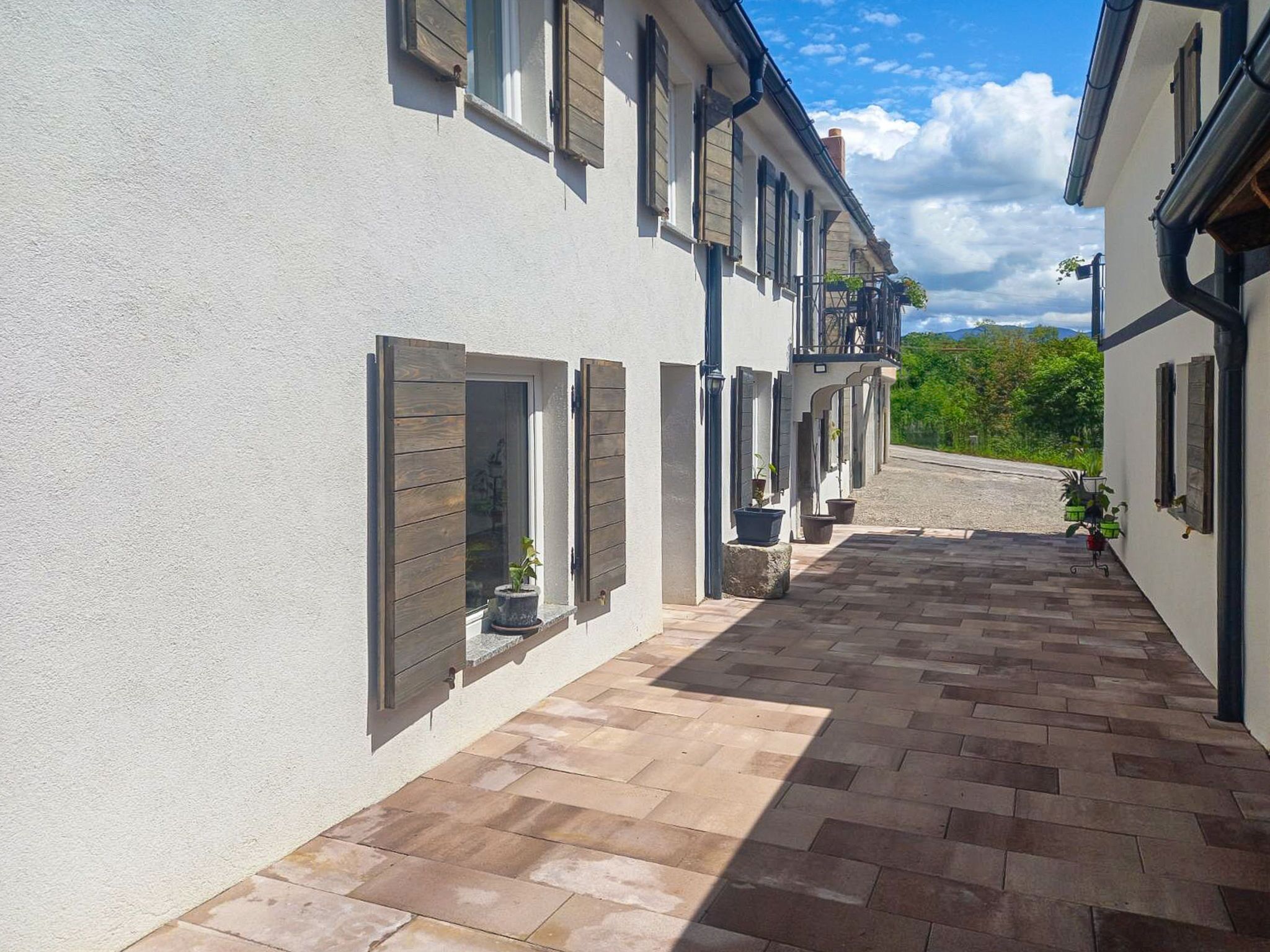 Une ruelle  étroite avec un trottoir pavé, bordée de bâtiments aux murs blancs et aux volets en bois.