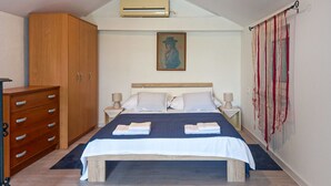 Un dormitorio con cama, dos mesitas de noche, un armario y un equipo de aire acondicionado.