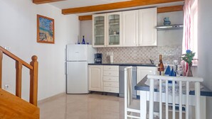 Una cocina con armarios blancos, un refrigerador blanco, una mesa de comedor con sillas y una escalera de madera.
