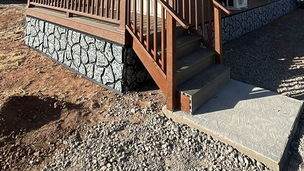 A two-story building with a stone foundation, wooden deck, and a covered porch with a railing.