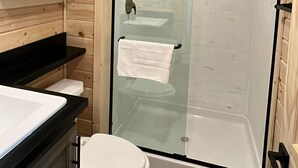 A wooden-paneled bathroom with a glass-enclosed shower, a white toilet, and a sink with a black countertop. - 064A Grand Canyon Chalet near South Rim With Loft (Williams)
