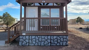A small cabin with a stone foundation, a wooden deck, and a clear sky in the background. - 064A Grand Canyon Chalet near South Rim With Loft (Williams)