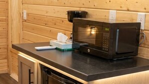 Une cuisine compacte équipée d’un four à micro-ondes encastré, d’un réfrigérateur et de murs recouverts de panneaux en bois.