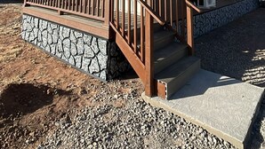Un bâtiment à deux étages, doté de fondations en pierre, d’une terrasse en bois et d’un porche couvert avec une balustrade.