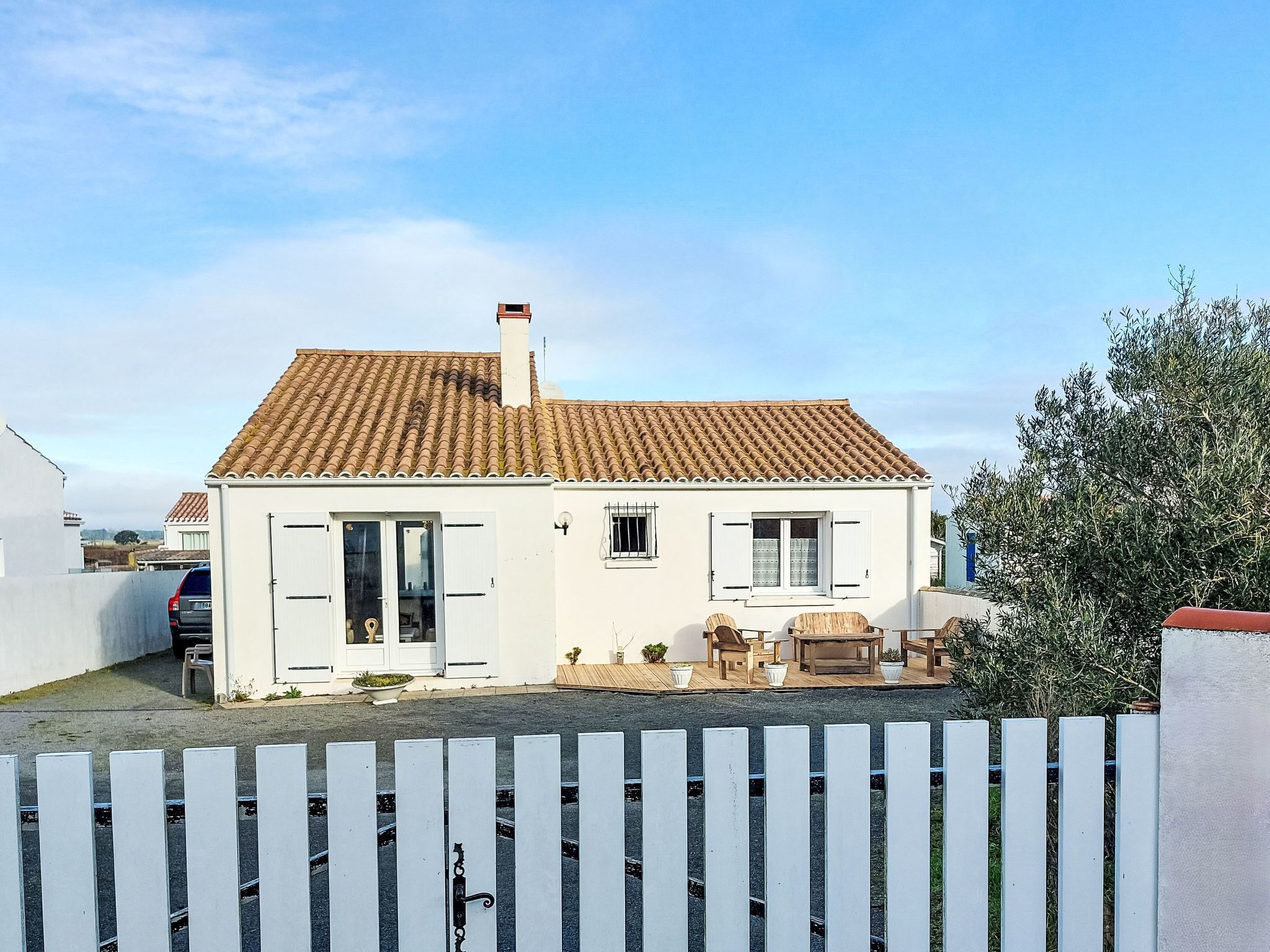 Une maison blanche avec un toit en tuiles, une porte d’entrée et un petit patio aménagé avec du mobilier d’extérieur.