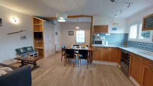 A modern kitchen with wooden cabinets, a dining area with a table and chairs, and a living room with a sofa and a TV. - Charme de la Petite Bosse by Interhome (Ile de Noirmoutier)
