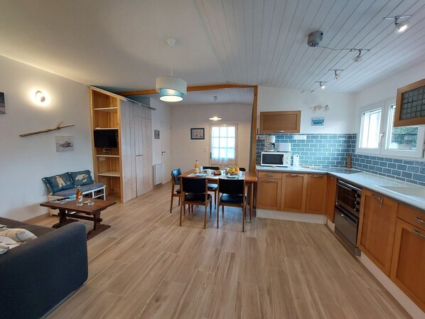 Una cocina moderna con armarios de madera, un comedor con mesa y sillas, y una sala de estar con sofá y televisor.