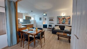 A modern living room with a sofa, coffee table, and dining area. There is a kitchen in the background with a refrigerator and cabinets. - Charme de la Petite Bosse by Interhome (Ile de Noirmoutier)