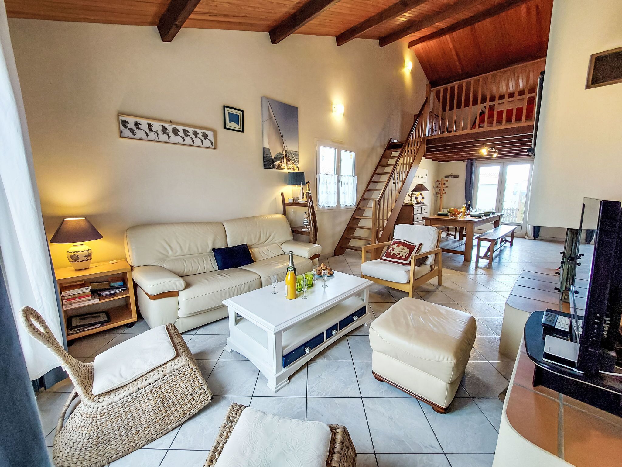 Un vaste espace de vie comprenant un canapé, une table basse et des fauteuils en osier. Un escalier mène à l’étage supérieur.