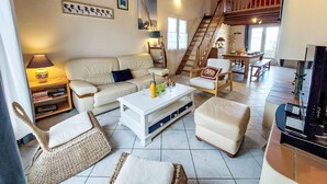 A spacious living area with a sofa, coffee table, and wicker chairs. A staircase leads to an upper level.