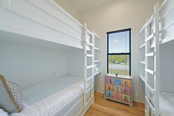 A child's bunk bed with white railings, a small wooden dresser with flip-flops, and a window with blinds. - Scarlett's Beach Heaven - Luxury Beach House with Rooftop Views and Pool (Miramar Beach)