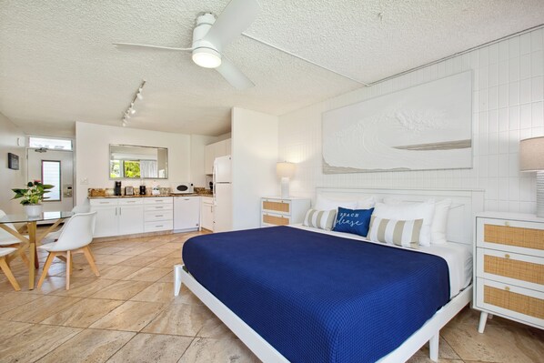 Quarto moderno com cama grande, paredes brancas e ventoinha de teto.