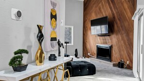 Una sala moderna con pared blanca y de madera, chimenea, televisor y sofá negro.