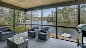 Un espacio de estar techado al aire libre con muebles de mimbre y vistas a un lago.