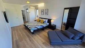 Een moderne slaapkamer met een groot bed, nachtlampjes, een bank en een spiegel.