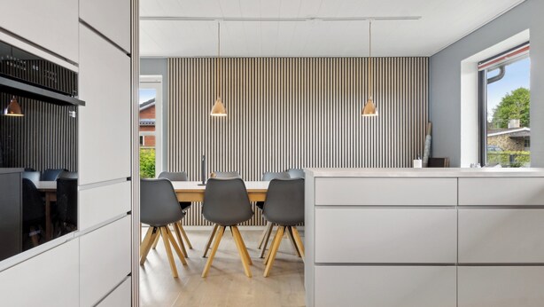 Eine moderne Küche mit Essbereich, ausgestattet mit einer gestreiften Wand, Pendelleuchten und Blick ins Freie.