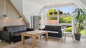 Ein modernes Interieur mit einer Wand aus Holzlatten, einer schwarzen Ledersofa, einem Holztisch und Blick auf Grünflächen im Freien.