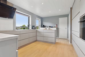 A modern kitchen with a large island, built-in appliances, and a view of the outdoors. - Near beach and golf with multi-purpose room (Farsø)