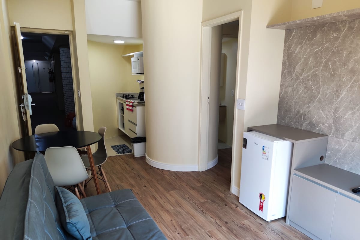 A compact living space with a sofa, a small dining table, a kitchenette, and a refrigerator.