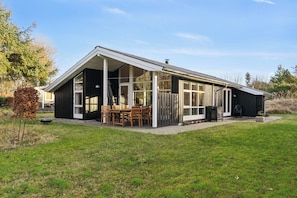Une maison moderne dotée d’un patio couvert, de grandes fenêtres et d’une cour gazonnée.