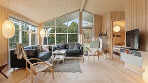 Ein geräumiges Wohnzimmer mit großem Fenster, einer Couch, einem Couchtisch und einem Fernseher.