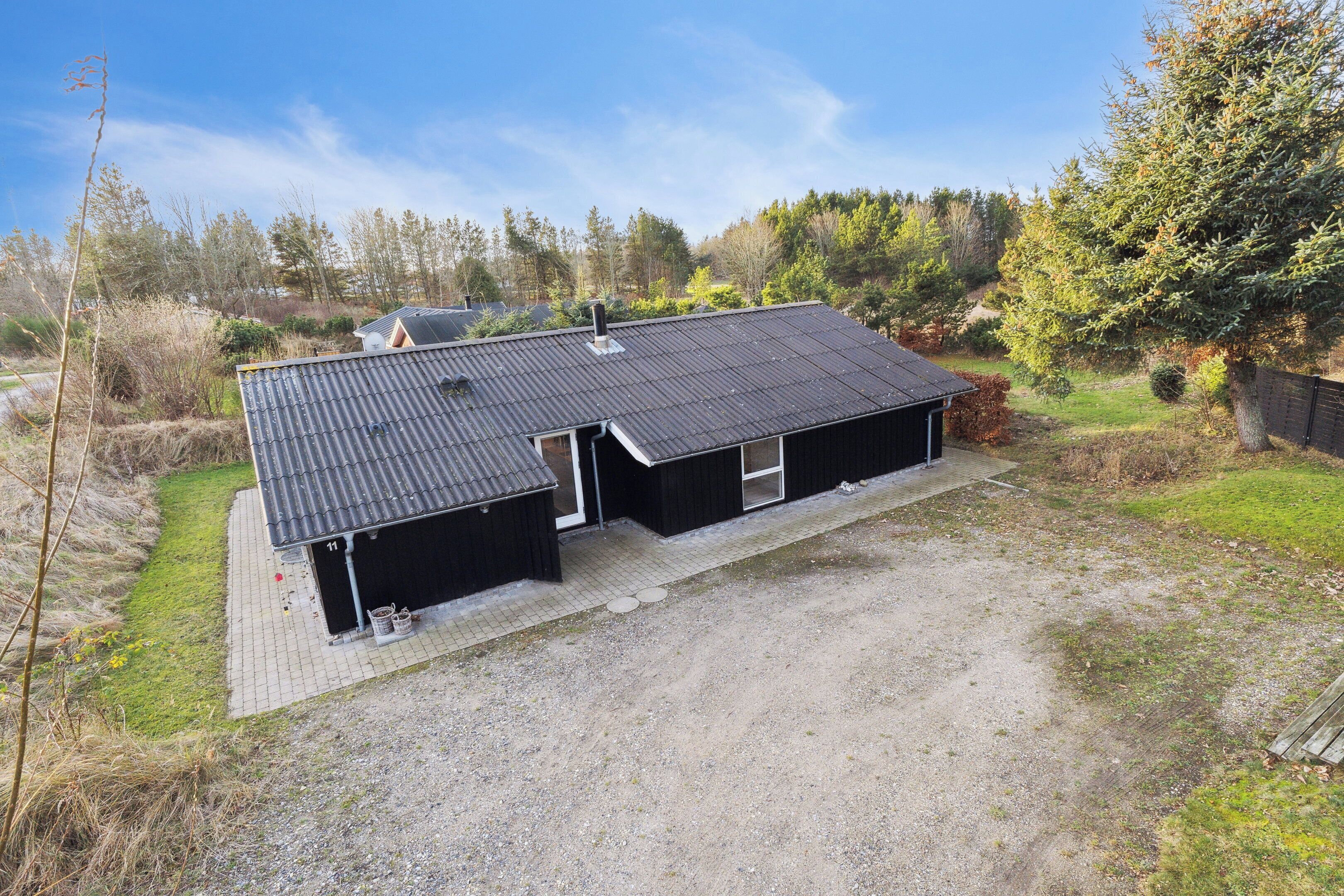 A two-story building with a metal roof, a gravel driveway, and a fenced yard.