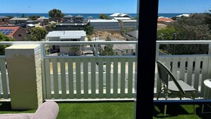 A balcony with a white picket fence, a chair, and a view of a coastal area with houses and the sea. - Beachfront apartment with pool & ocean views, 4 mins walk to Beach. Sleeps 7 (Quinns Rocks)
