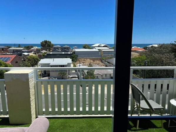 A balcony with a white picket fence, a chair, and a view of a coastal area with houses and the sea. - Beachfront apartment with pool & ocean views, 4 mins walk to Beach. Sleeps 7 (Quinns Rocks)