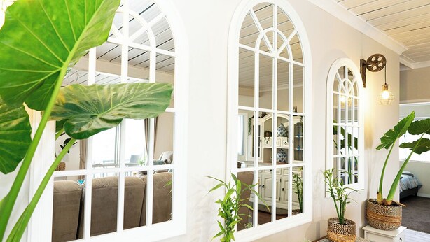 A room with large arched windows, a wooden table with potted plants, and a cozy seating area with cushions. - Beachfront apartment with pool & ocean views, 4 mins walk to Beach. Sleeps 7 (Quinns Rocks)