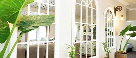 Una habitación con amplios ventanales de arco, una mesa de madera con plantas en macetas y un rincón de estar acogedor con cojines.