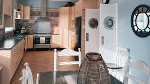 A modern kitchen with wooden cabinets, a stainless steel stove, and a dining area with a dark wooden table and white chairs. - Beachfront apartment with pool & ocean views, 4 mins walk to Beach. Sleeps 7 (Quinns Rocks)