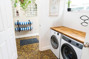A laundry room with a washing machine, a wooden countertop, a blue and white towel rack, a potted plant, and a motivational poster.